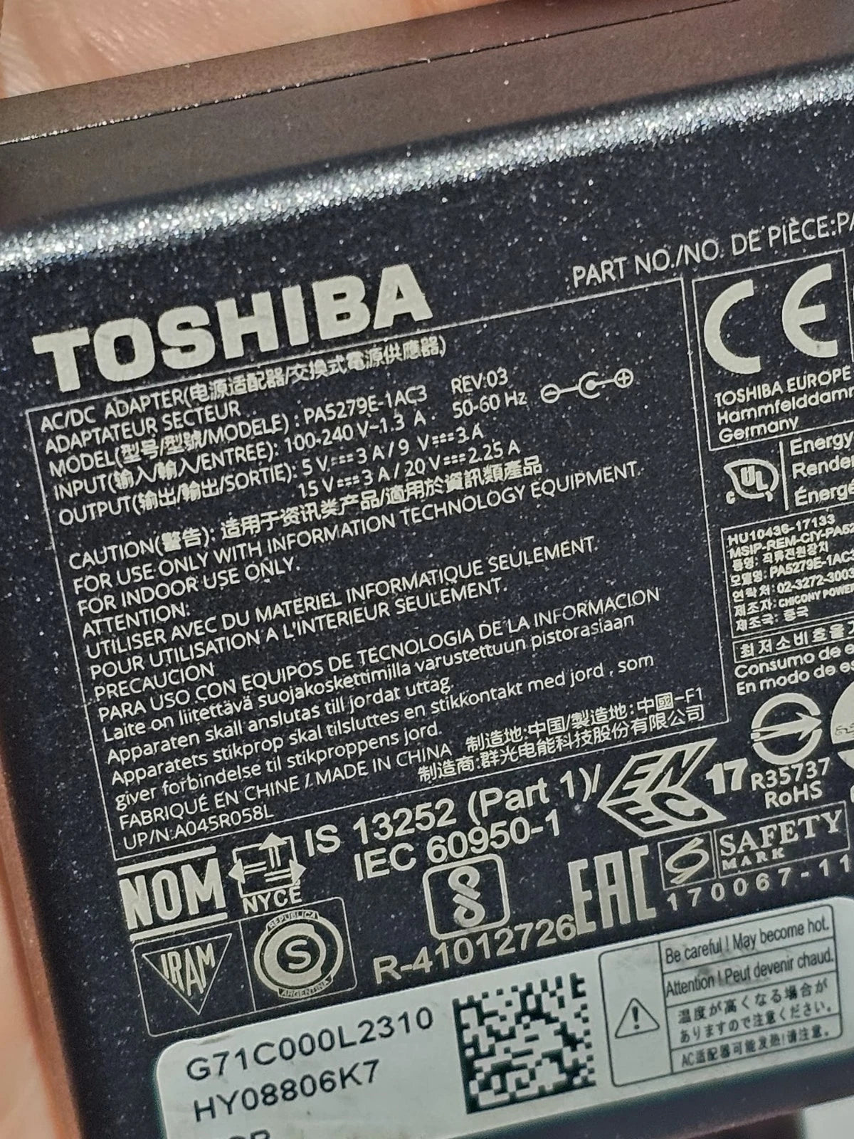 Toshiba AC adapter with various certification logos and text on a metallic surface.